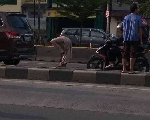 Seorang pria melakukan gerakan sholat di tengah jalan