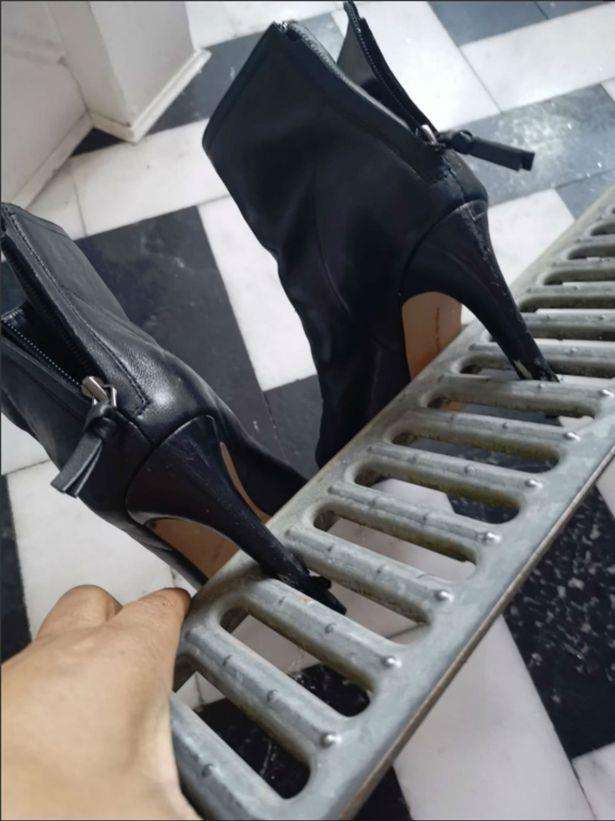 Sepatu high heels terjepit terali penutup saluran pembuangan air.