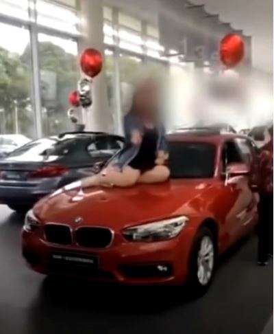 Wanita duduk di atas kap mobil.