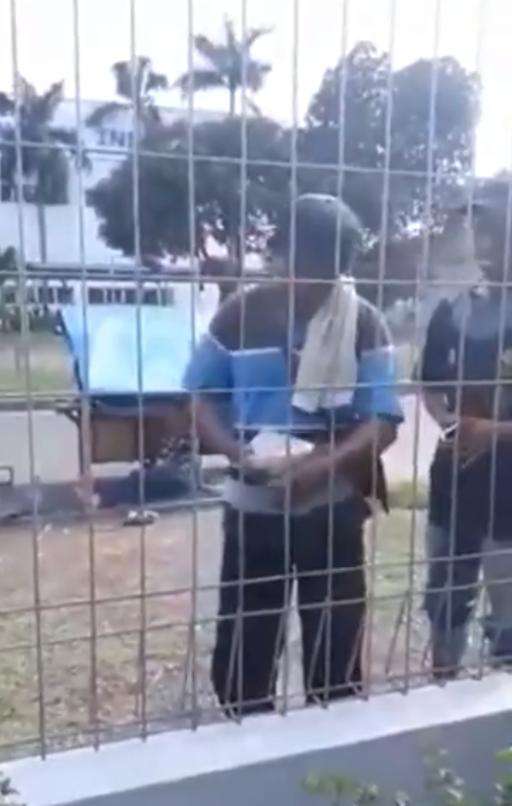 Tukang bubur terhalang pagar tiinggi saat melayani pembeli.