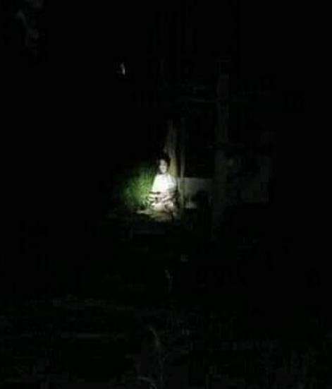 Penampakah sosok perempuan duduk sambil senyum di tempat gelap.