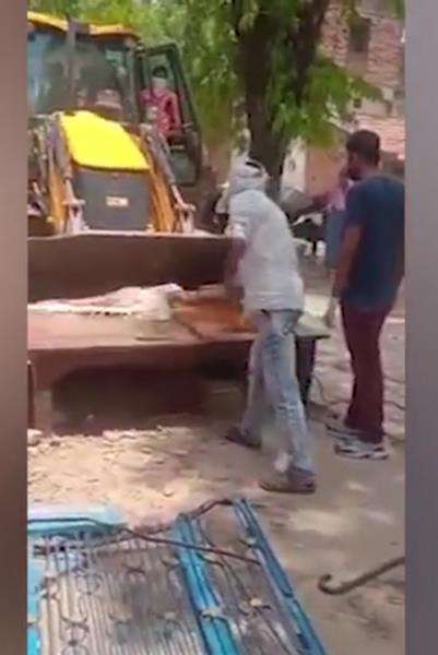 Warga menggunakan kayu untuk mendorong jenazah korban Covid-19 ke ekskavator.