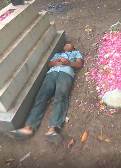 Aksi nyeleneh pria tidur di samping kuburan.