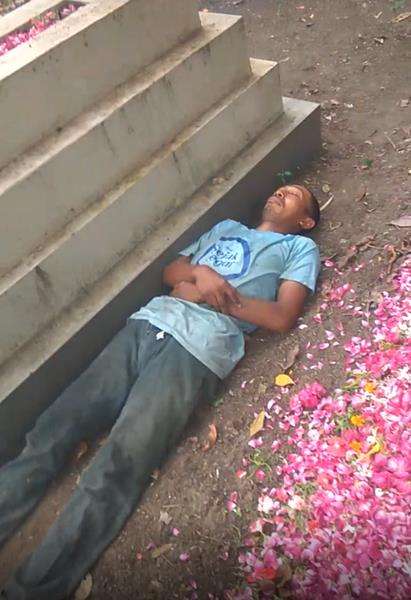 Aksi nyeleneh pria tidur di samping kuburan.
