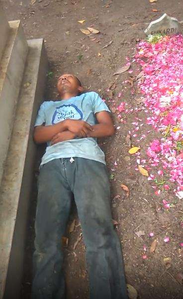 Aksi nyeleneh pria tidur di samping kuburan.