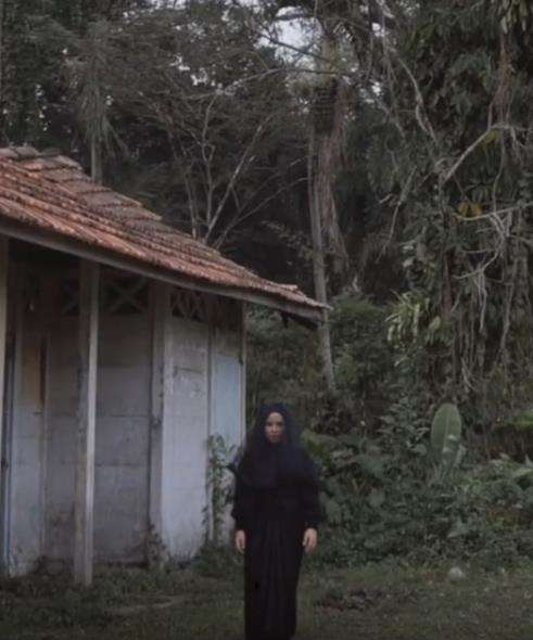 Gadis bergaun dan berkerudung hitam dekat rumah reyot pinggir hutan.