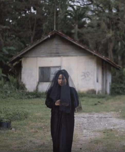 Gadis bergaun dan berkerudung hitam dekat rumah reyot pinggir hutan.