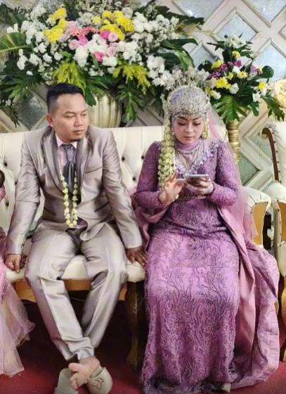 Sambil gendong anak istri tua dampingi suami duduk bersama istri muda di pelaminan.
