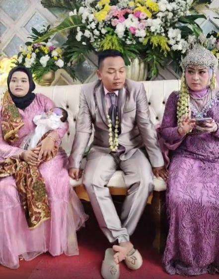 Sambil gendong anak istri tua dampingi suami duduk bersama istri muda di pelaminan.