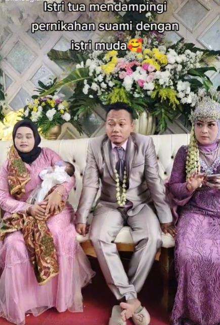 Sambil gendong anak istri tua dampingi suami duduk bersama istri muda di pelaminan.