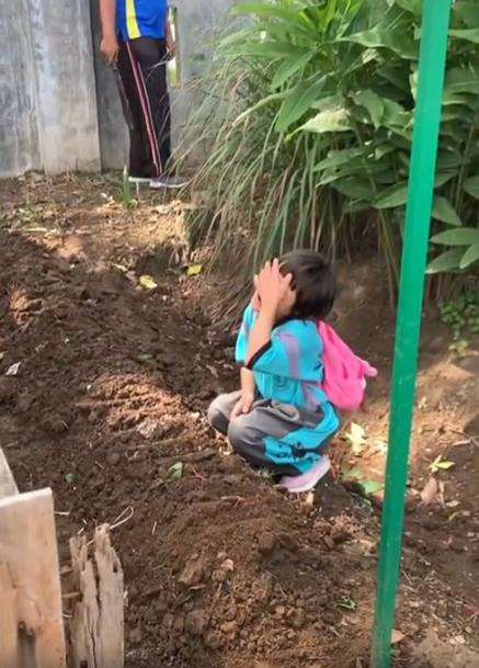 Bocah berdoa di samping gundukan tanah.