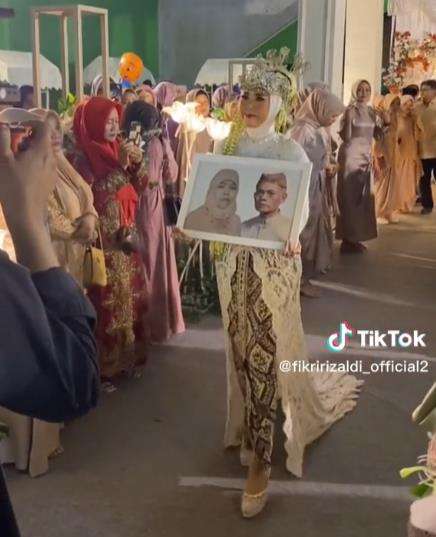 Pengantin wanita bawa foto orangtua di hari pernikahannya.