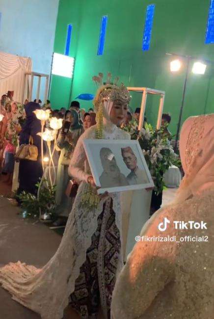 Pengantin wanita bawa foto orangtua di hari pernikahannya.
