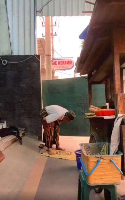 Penjual sate tengah sholat di belakang gerobaknya.