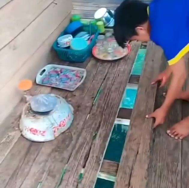 Tak sangka di bawah lantai rumah reyot dari papan ini ada kolam ikannya.